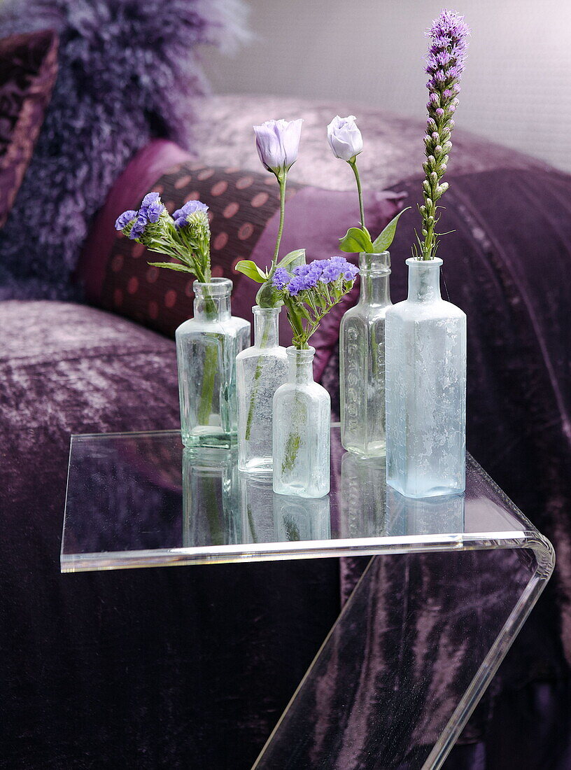 Medicine bottles with single stem flowers on table beside purple bedspread renovated Cotswolds mill house England UK
