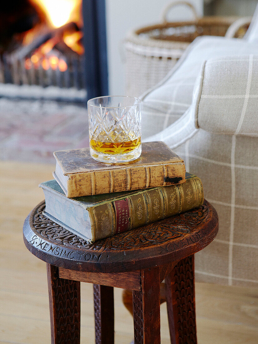 Whiskyglas und Bücher auf geschnitztem Beistelltisch im Wohnzimmer eines Hauses in Hampshire England UK