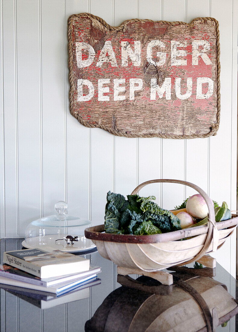 "Gartenteppich und Bücher auf polierter Küchentheke mit einem Schild Danger Deep Mud"" (Gefahr tiefer Schlamm) in Hampshire, England, UK"""