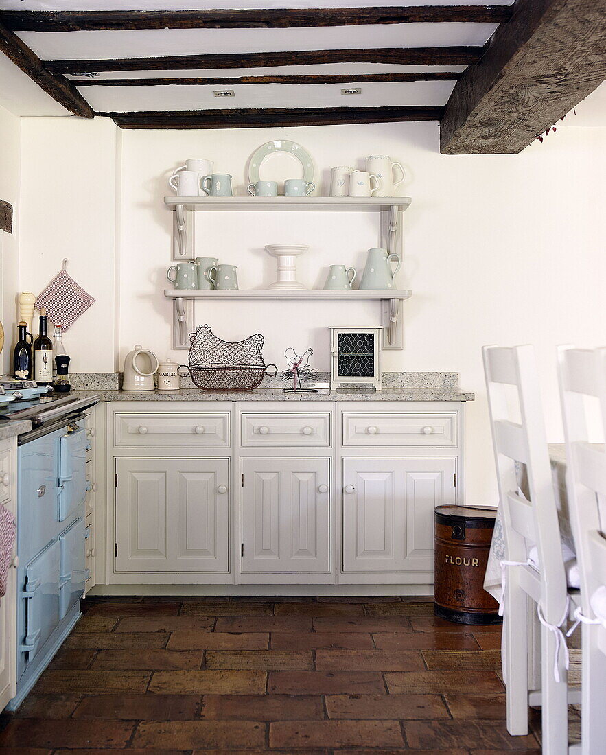 Crockery on shelving with fitted units in beamed kitchen of Forest Row farmhouse Surrey England UK