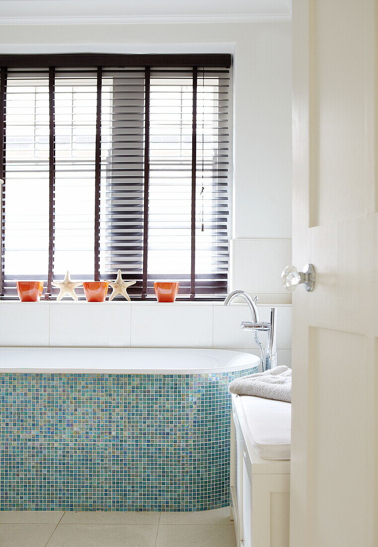 Turquoise mosaic tiled bath below window with louvered blinds in Harrogate home Yorkshire England UK