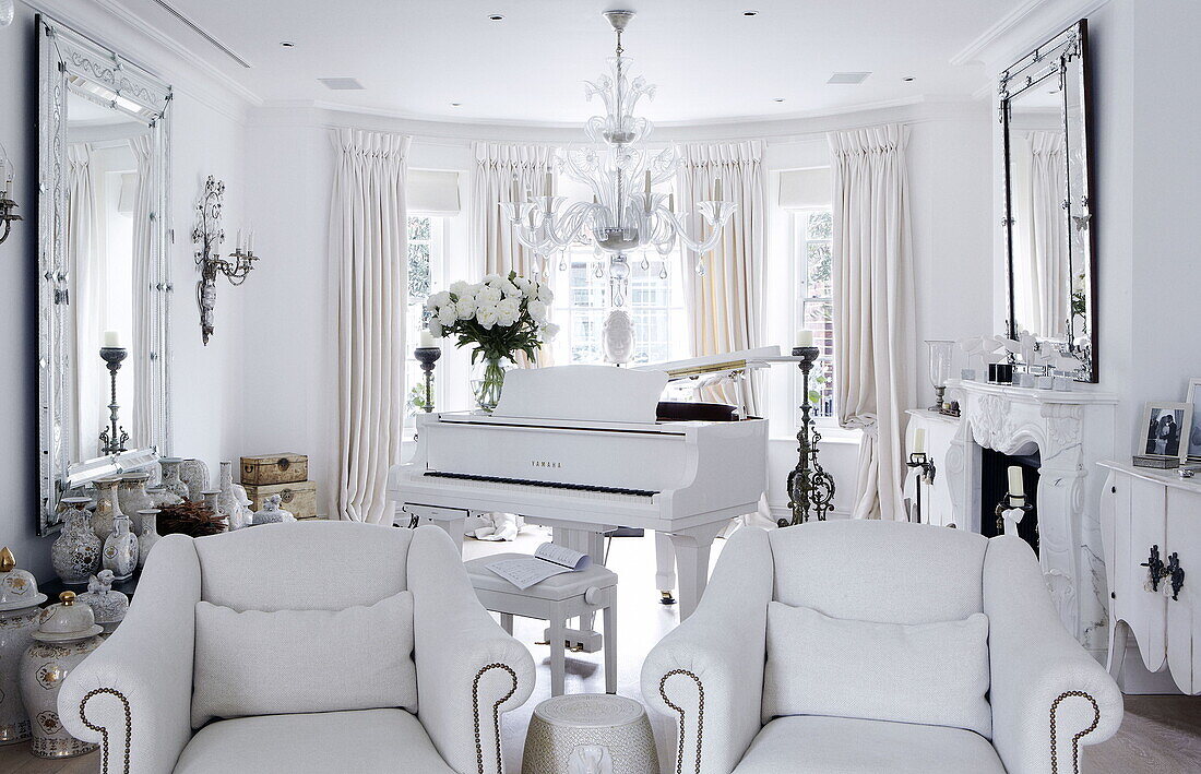 Grand piano and matching white armchairs with a collection of vases London home UK
