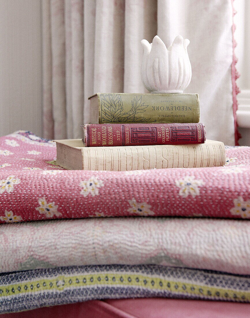 Hardbacked books on folded bed quilts in London home UK
