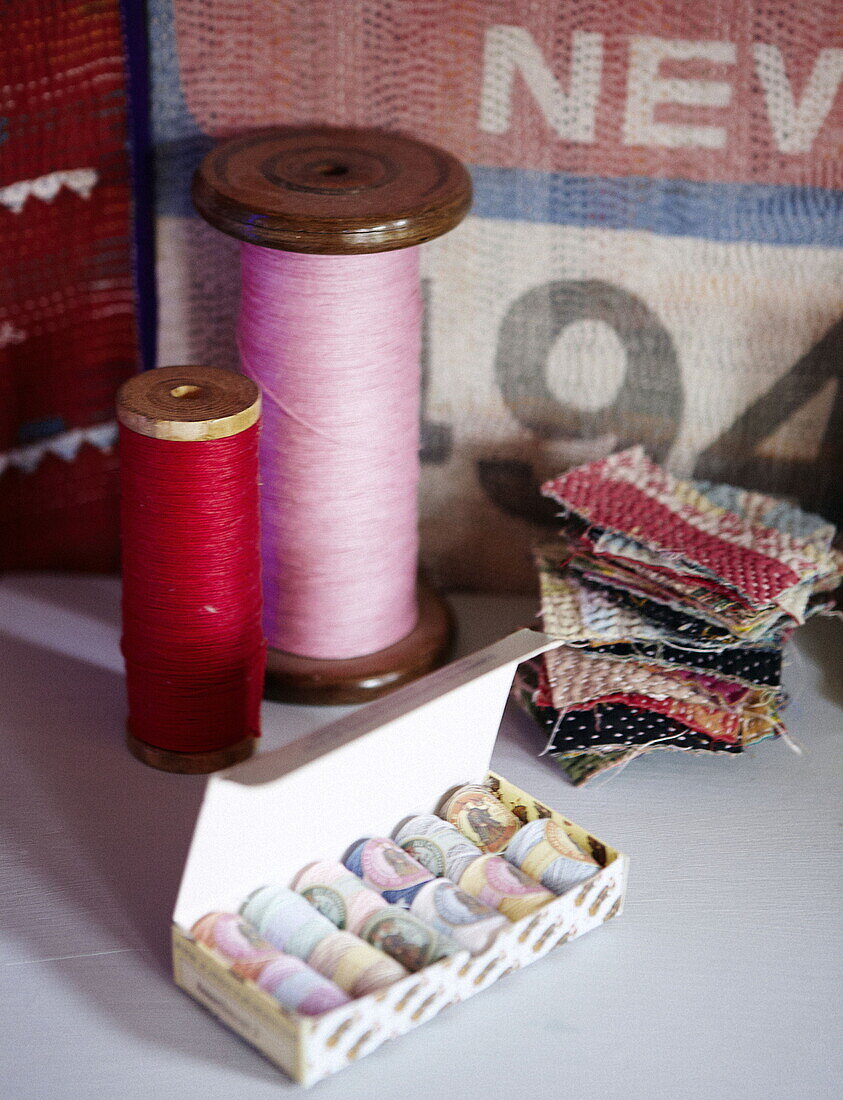 Pink and red thread on vintage bobbins with fabric samples in home of London textiles designer UK
