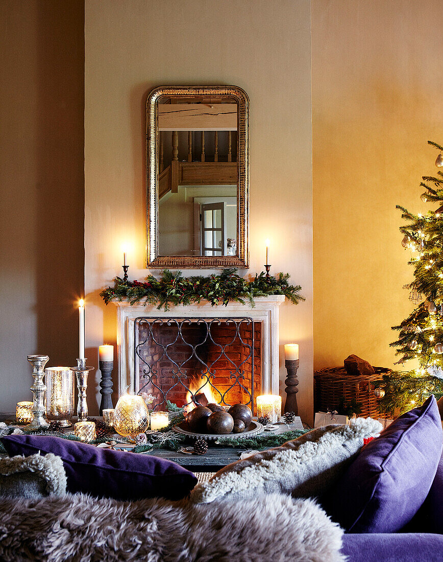 Purple cushions on sofa with mirror above mantlepiece and lit fire in festive Oxfordshire home, England, UK