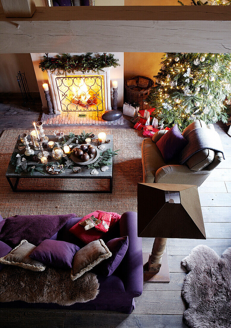 Erhöhte Ansicht des Weihnachtsbaums und des violetten Sofas am beleuchteten Feuer in einem festlichen Haus in Oxfordshire, England, UK