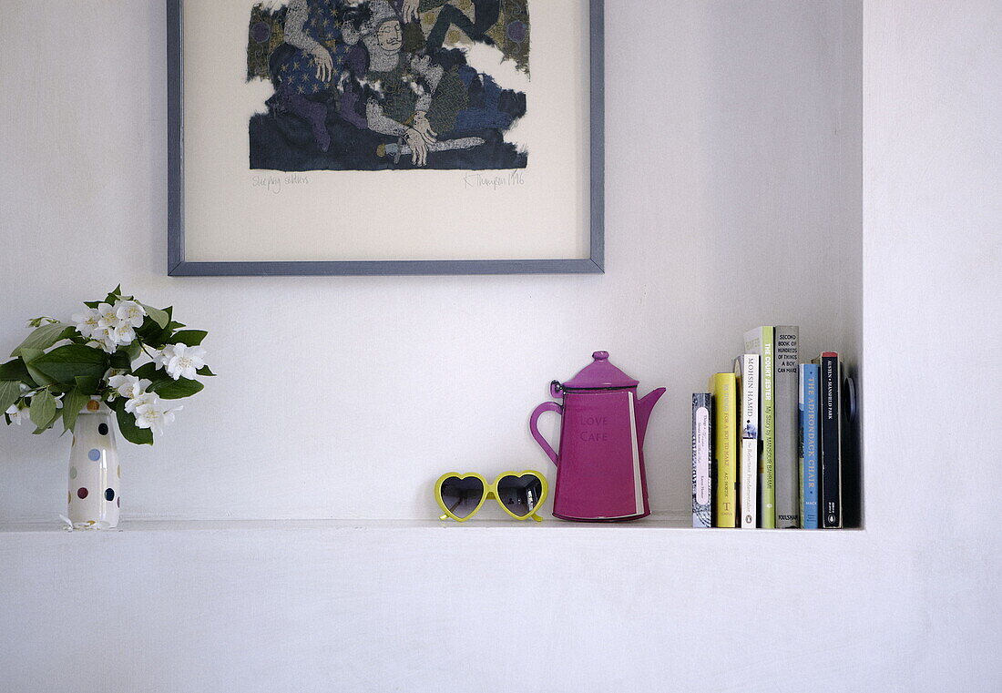 Bücher und rosa Kaffeekanne mit Schnittblumenvase auf Alkovenregal in Londoner Familienhaus UK