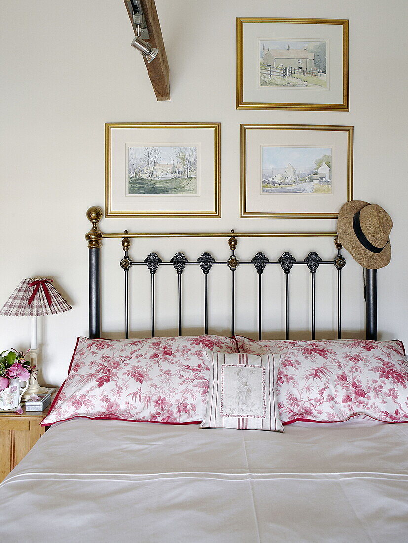 Schlafzimmer mit floralen Mustern und Kopfteil aus Messing mit Kunstwerken in einem Landhaus in Hexham, Northumberland (England)