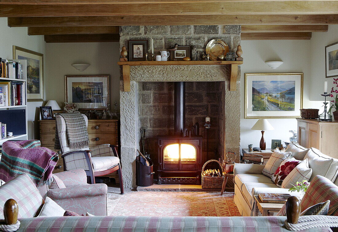 Lit woodburner in exposed stone fireplace with seating area in Hexham country house Northumberland England UK