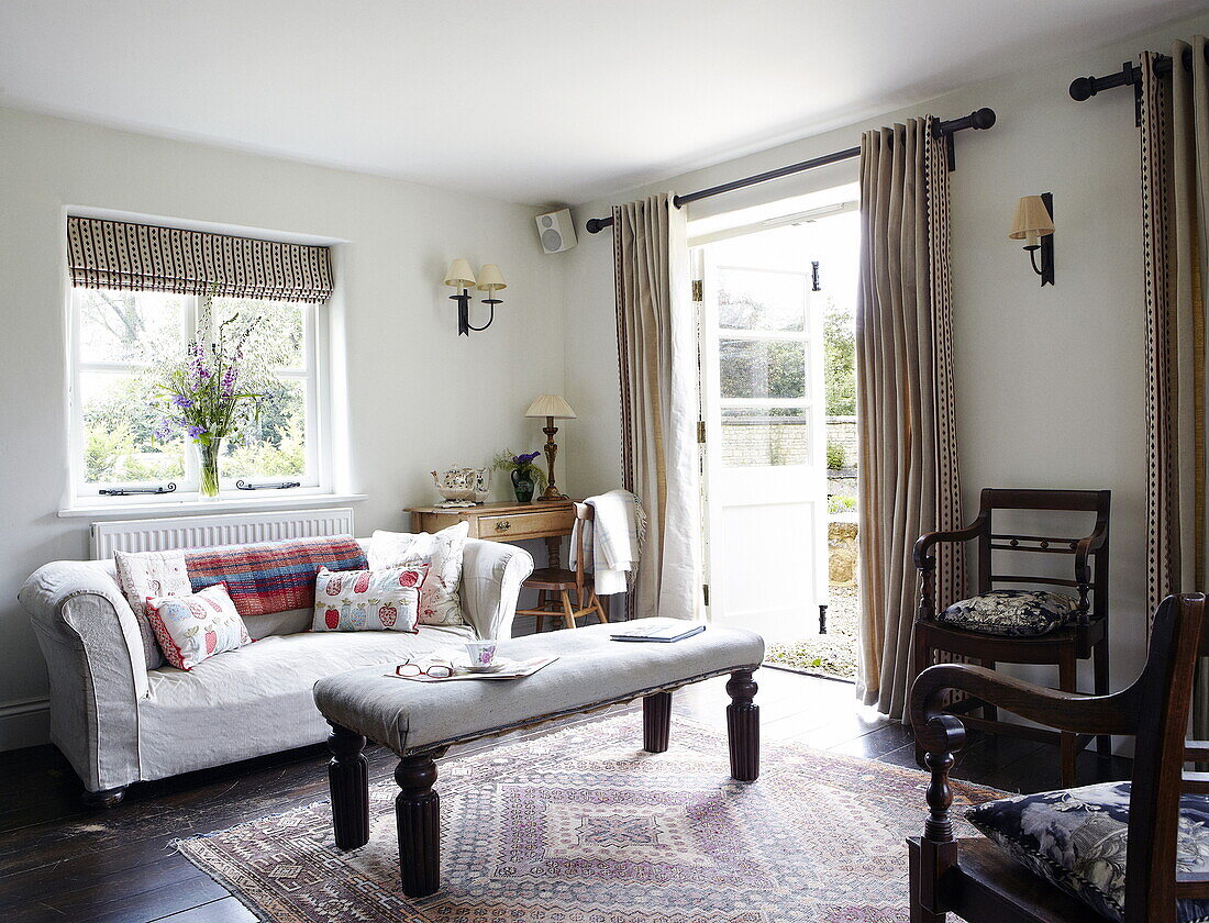 Gepolsterter Schemel und Esszimmerstühle mit Sofa im Wohnzimmer eines Hauses in Oxfordshire, England, UK