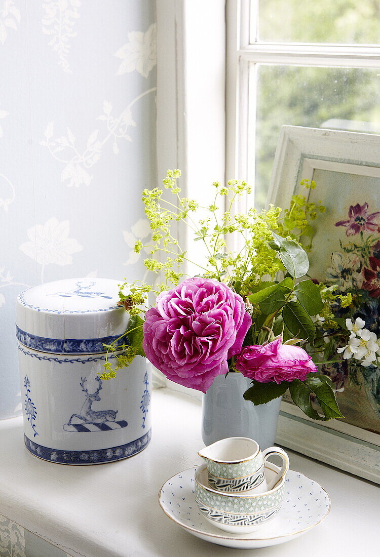 Cut flowers and storage jar with teacup on windowsill in Oxfordshire home, England, UK