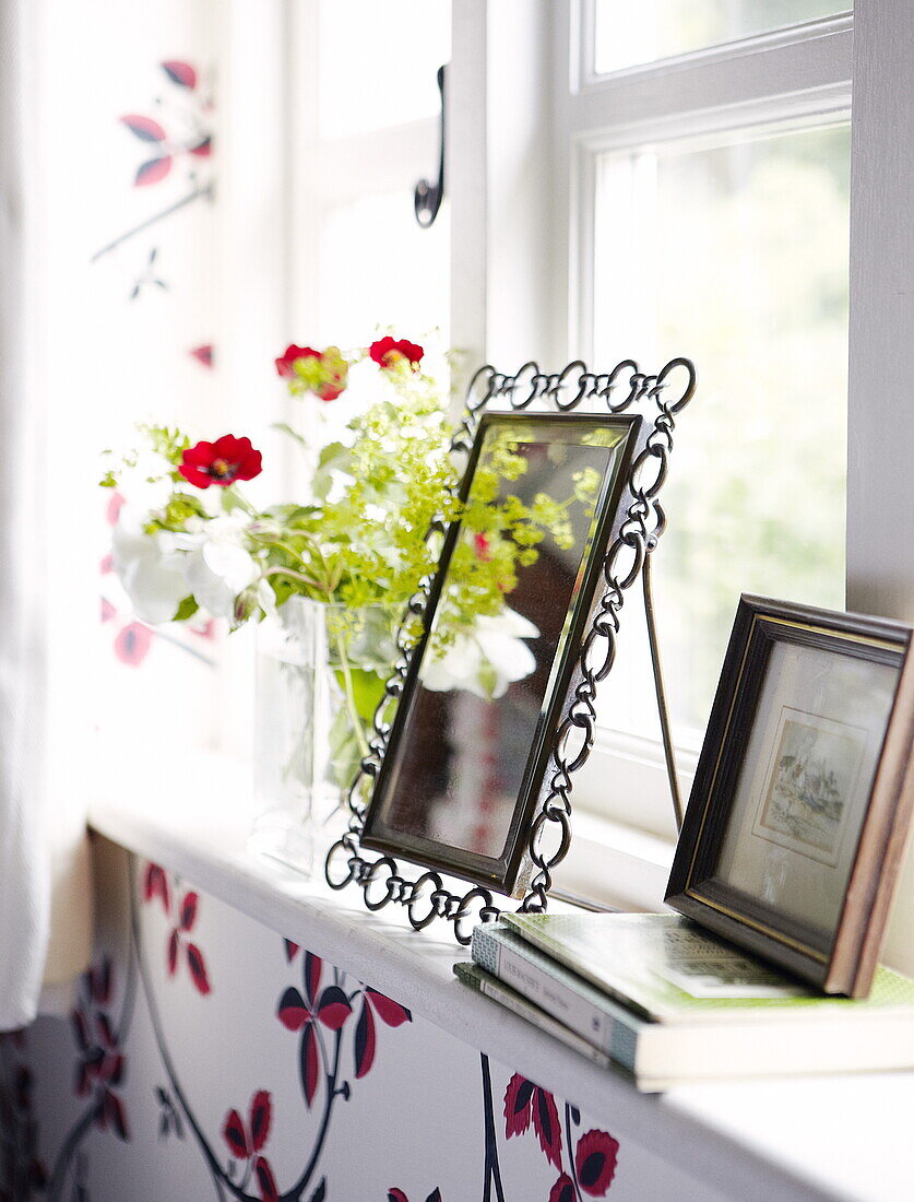 Gerahmte Bilder und Schnittblumen auf der Fensterbank eines Hauses in Oxfordshire, England, UK