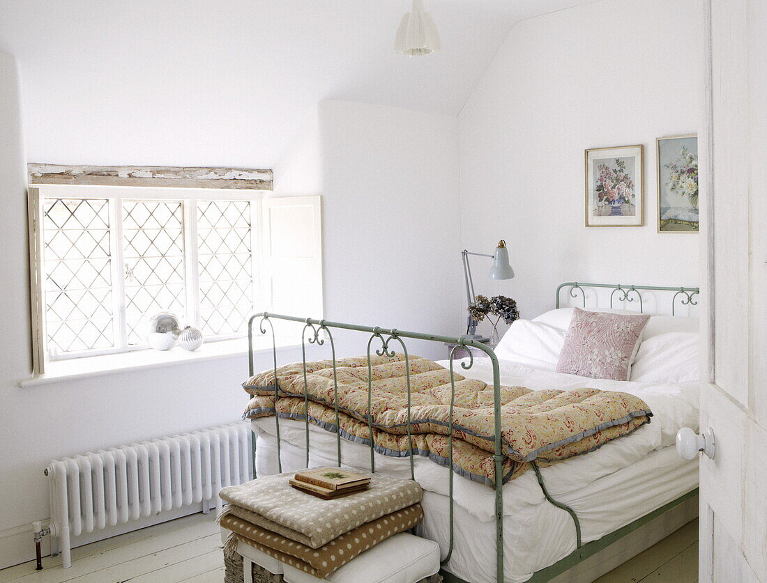 Bett mit Metallrahmen, Steppdecke und Bleiglasfenster in einem Schlafzimmer in einem Cottage in Oxfordshire, England, Vereinigtes Königreich