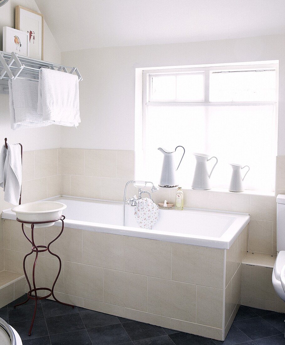 Jugs on windowsill in cream and white bathroom with antique wash stand in Staffordshire home, England, UK