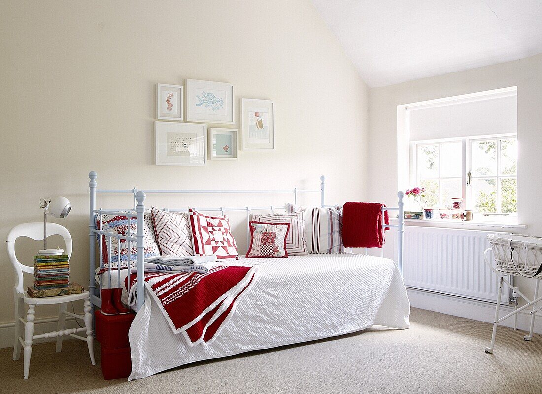 Blue daybed with red cushions and blankets below artwork in contemporary Staffordshire home, England, UK