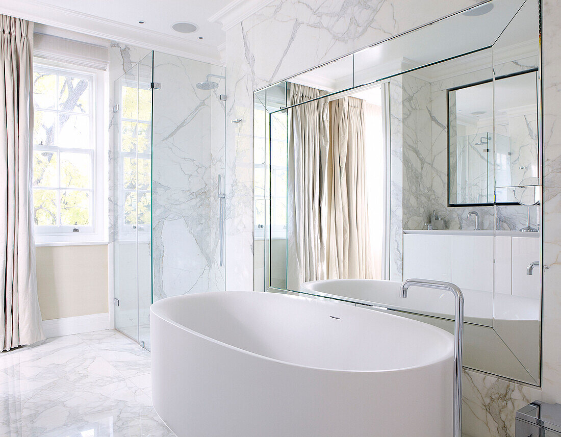 Freistehende Badewanne in einem Marmorbad mit großem Spiegel, der das Licht reflektiert, Haus in London, England, UK