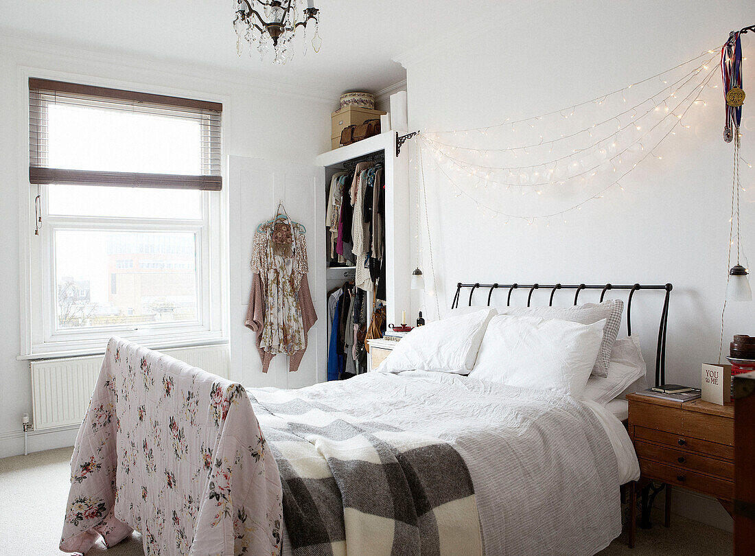 Lichterkette über einem ungemachten Bett mit grau-karierter Decke und geblümter Steppdecke in einem modernen Haus, Hastings, East Sussex, UK
