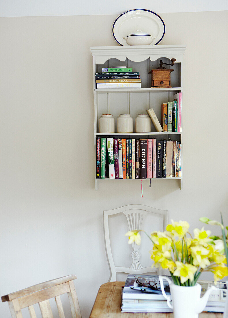 Wall mounted bookcase with crockery and daffodils in Warwickshire home, England, UK