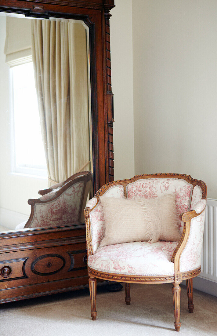 Upholstered antique armchair with mirrored wardrobe in Warwickshire home, England, UK