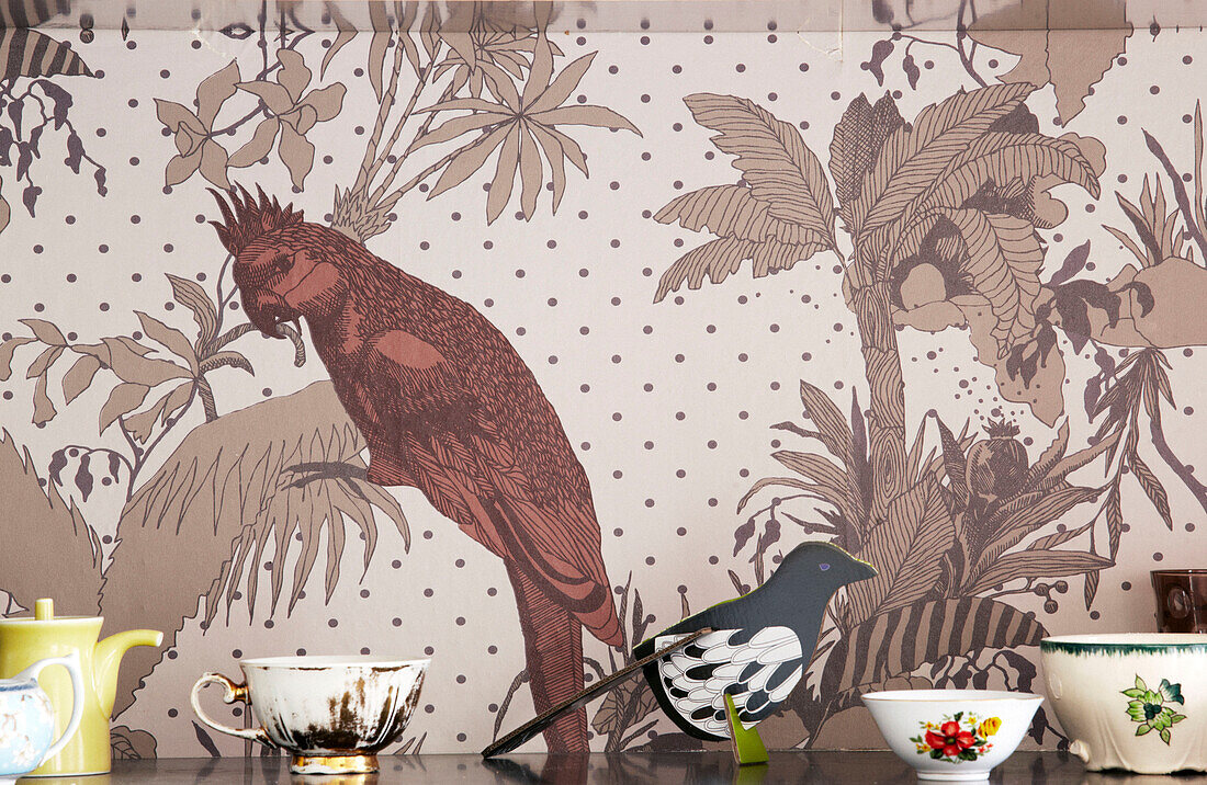 Chinaware and model bird set against parakeet wallpaper in contemporary apartment, Amsterdam, Netherlands