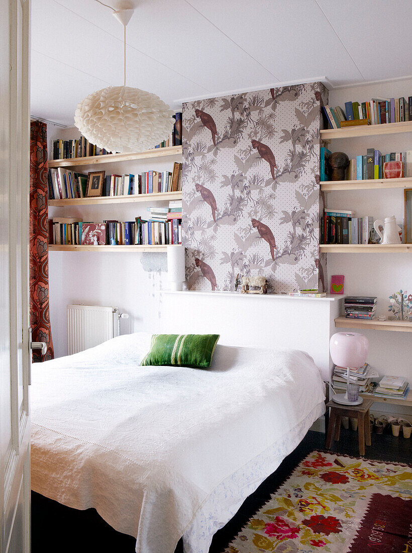 Bookshelves above double bed with white bed cover in contemporary family home, Amsterdam, Netherlands