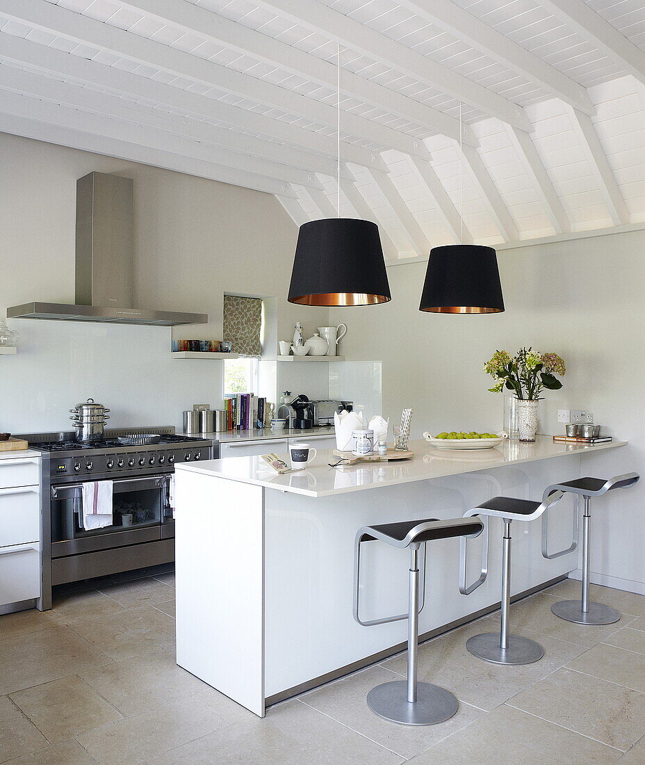 Open plan kitchen with black pendant lamps and bar stools at breakfast bar, Oxfordshire, England, UK