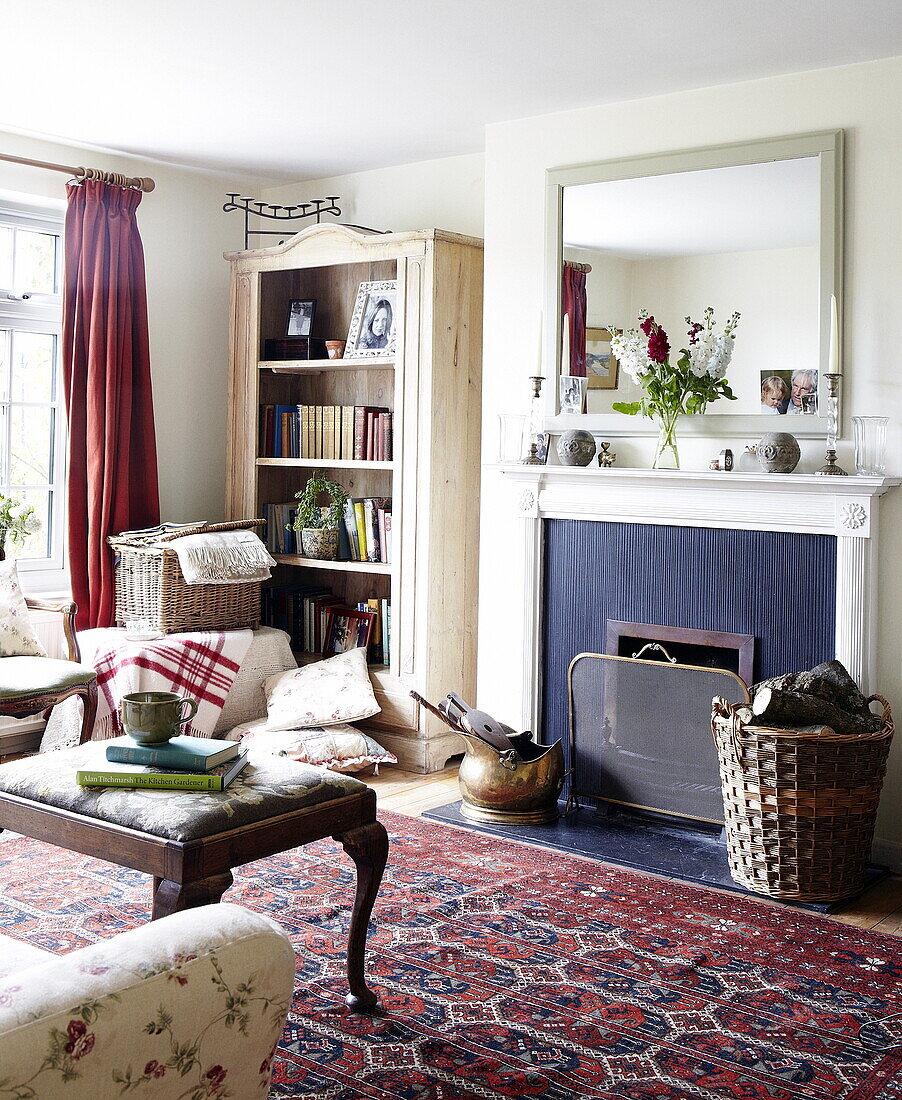 Firewood and bookshelf in living room with patterned rug and mirror over fireplace, Oxfordshire, England, UK