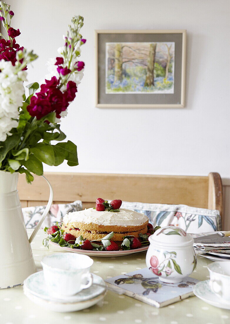 Erdbeer-Biskuitkuchen und Schnittblumen mit Teetasse und Zuckerdose auf dem Tisch, Oxfordshire, England, UK
