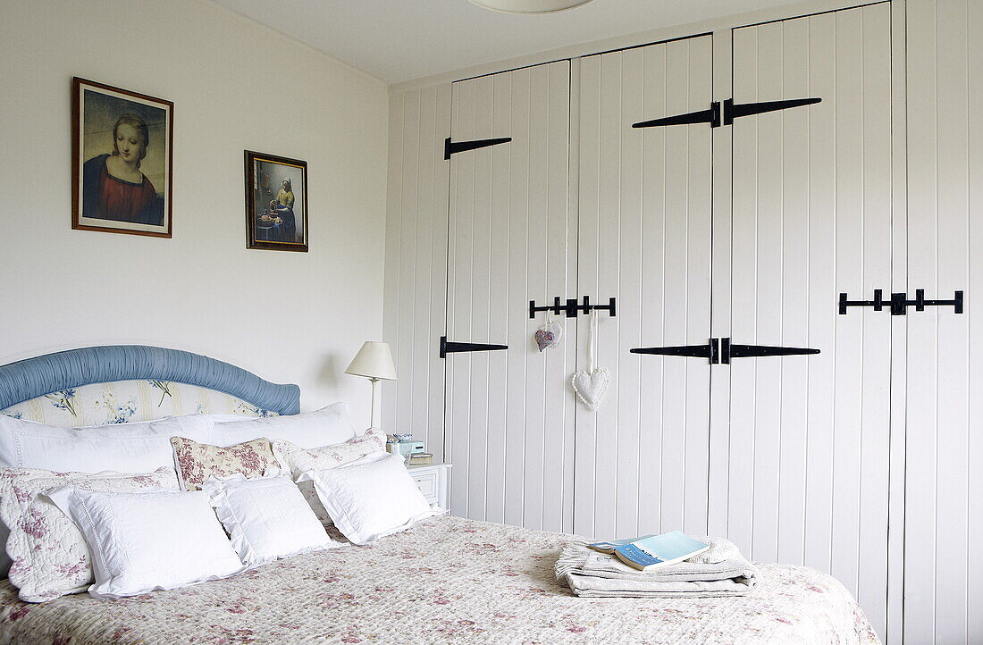 Blaues Kopfteil auf einem gesteppten Bett in einem Schlafzimmer mit weiß gestrichenen und aufklappbaren Einbauschränken, Oxfordshire, England, UK
