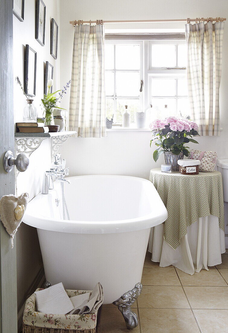Freistehende Badewanne mit Regal und Kunstwerk am Fenster in einem Landhaus, Oxfordshire, England, UK
