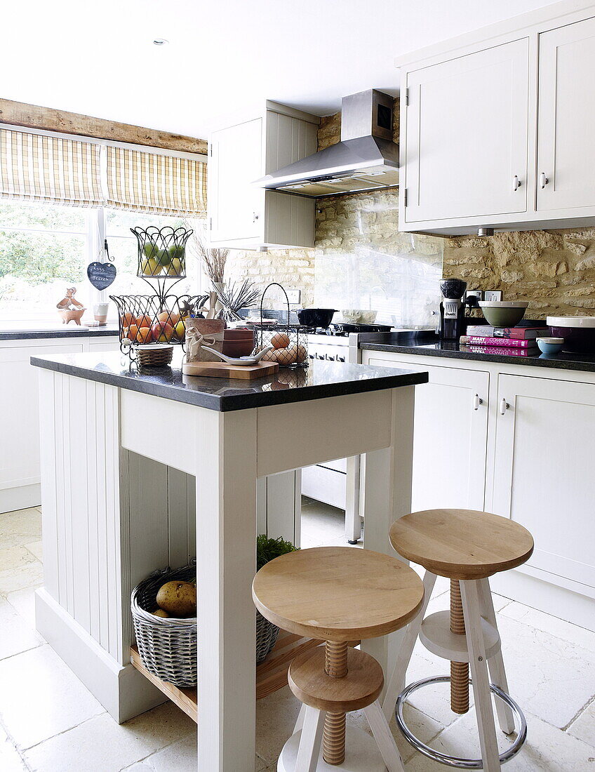 Wooden stools at kitchen island in kitchen of barn conversion in Oxfordshire, England, UK