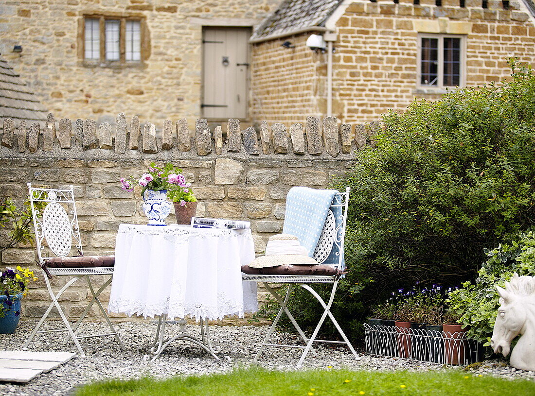 Tischdecke aus Spitze und Stühle für zwei Personen im Garten neben der Steinmauer eines Hauses in Oxfordshire, England, UK
