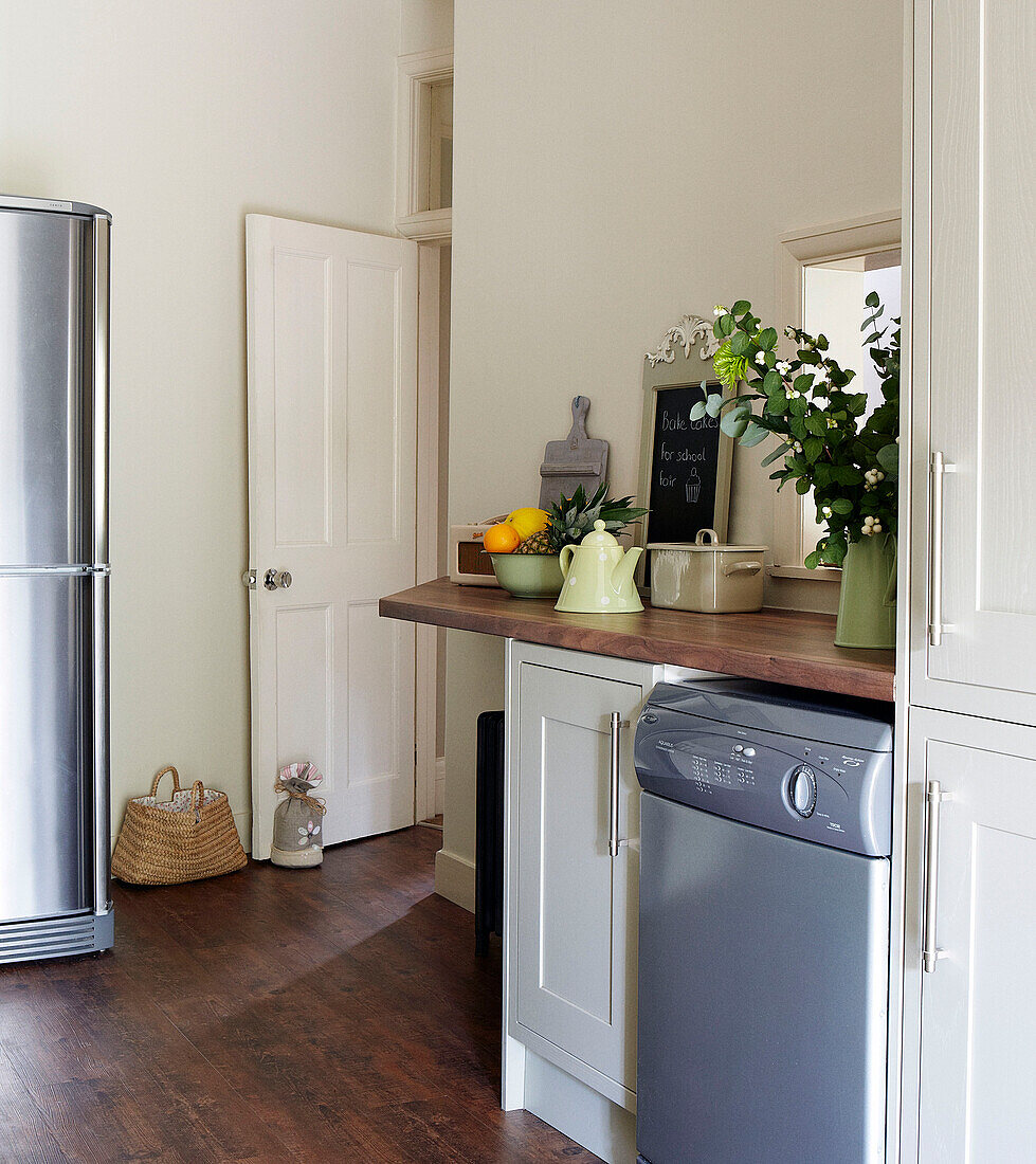 Upright fridge and dishwasher in kitchen with door held open with doorstop in North London home, England, UK