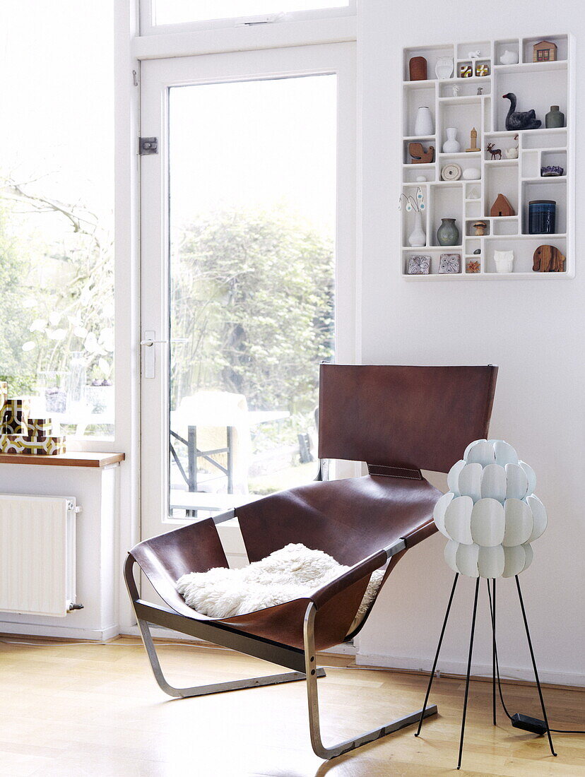 Brown leather retro armchair with wall mounted shelving at glass back door in Bussum home, Netherlands