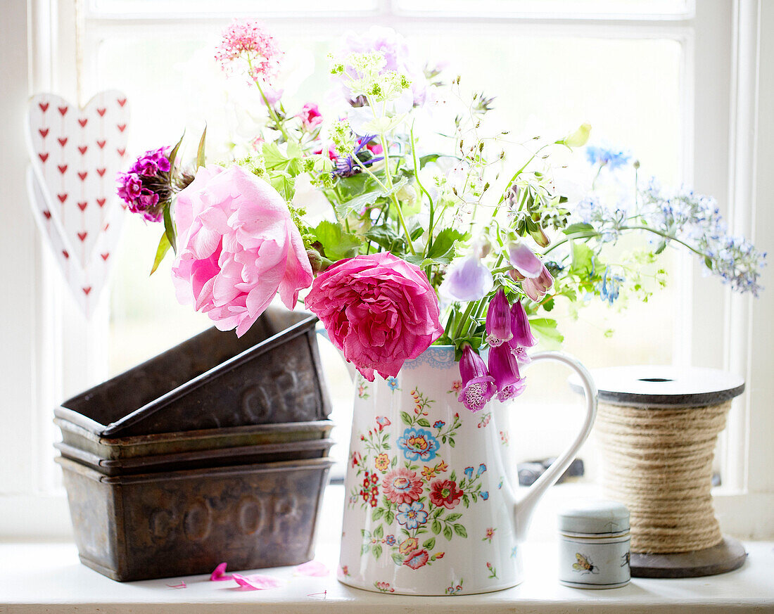 Cut flowers on windowsill of Surrey farmhouse with vintage baking tins and rope England UK