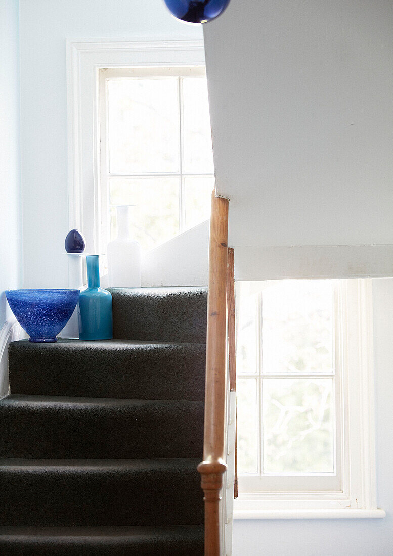 Blue glassware on grey staircase with wooden handrail London townhouse England UK