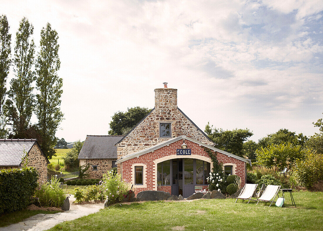 Liegestühle und Grill im Garten einer umgebauten Schule in der Bretagne mit Backsteinanbau Frankreich