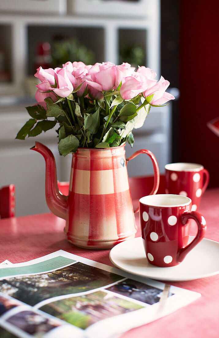 Pink roses in metal jug with red and white spotty mugs in kitchen of schoolhouse conversion Brittany France