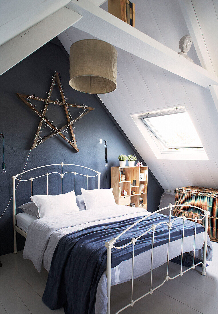 Wooden star above white framed double bed in attic of schoolhouse conversion Brittany France
