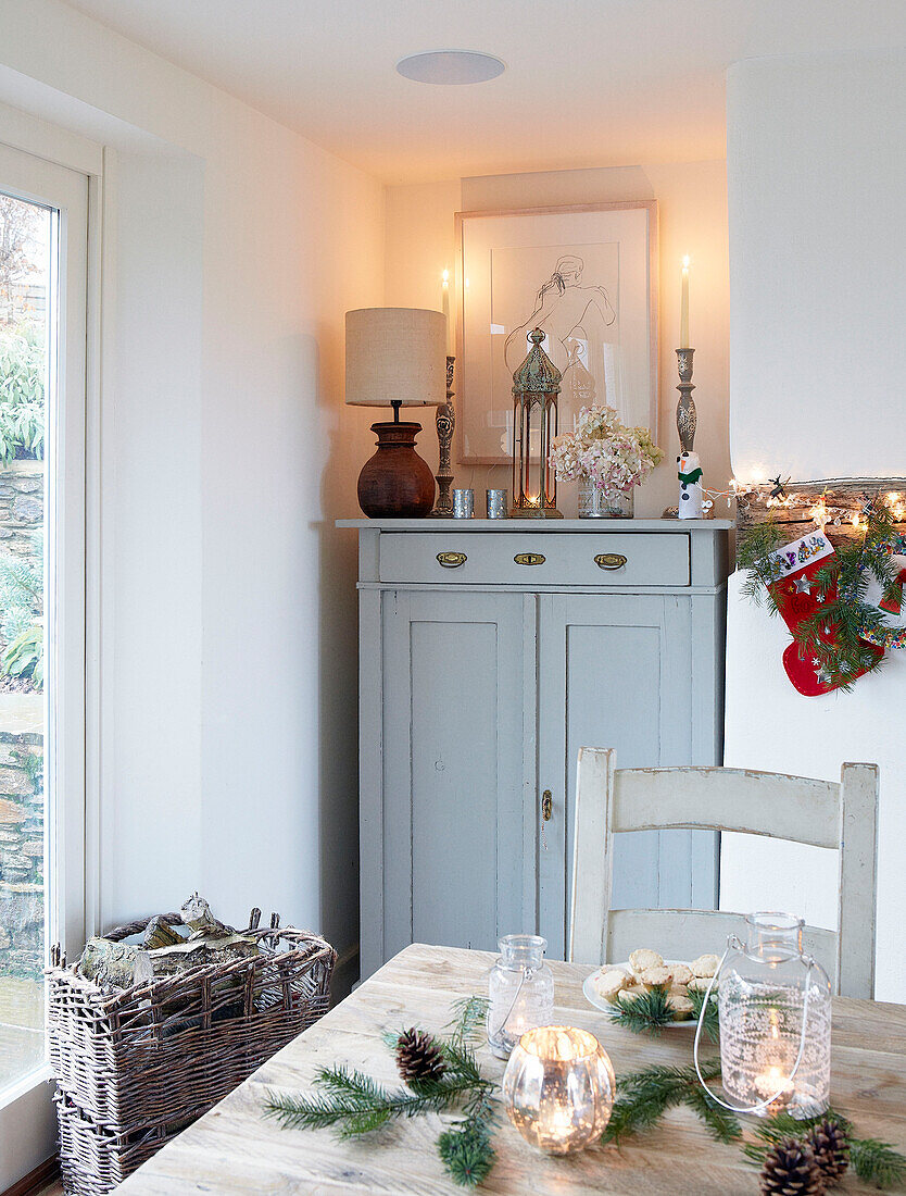 Kieferndekoration auf hölzernem Küchentisch in einem Raum mit Holzkorb und bemalten Schränken in einem Haus in Devonshire, UK
