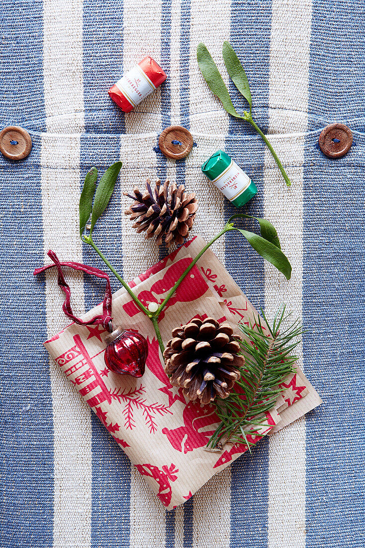 Tannenzapfen und Mistelzweig mit Weihnachtsserviette auf gestreiftem Stoff mit Holzknöpfen in einem Landhaus in Devonshire