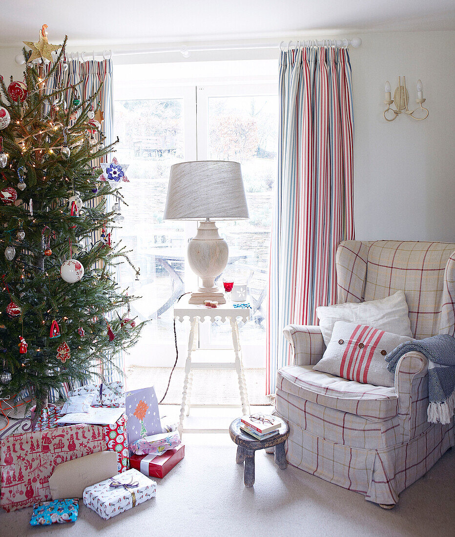 Weihnachtsbaum und Sessel mit Lampe auf dem Tisch am Fenster eines Landhauses in Devonshire UK