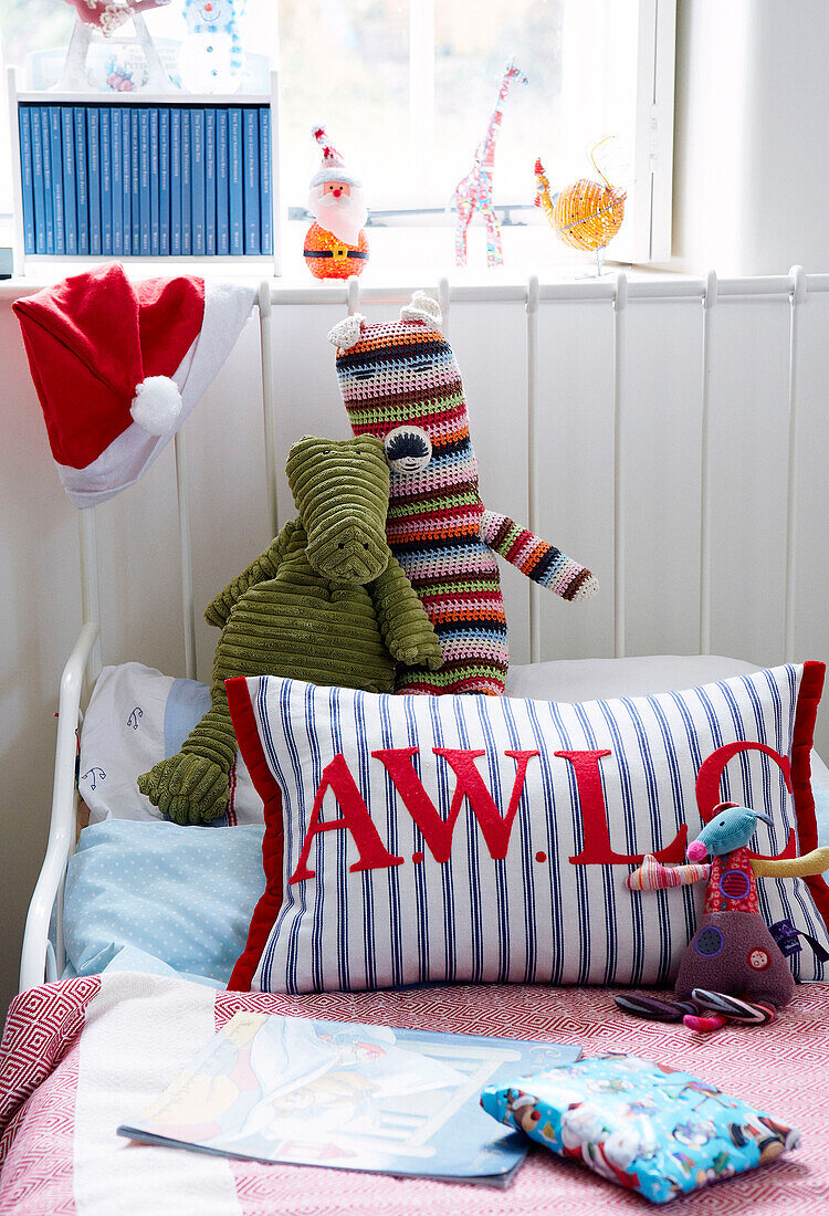 Stofftiere und monogrammiertes Kissen auf dem Bett im Kinderzimmer eines Landhauses in Devonshire, Großbritannien