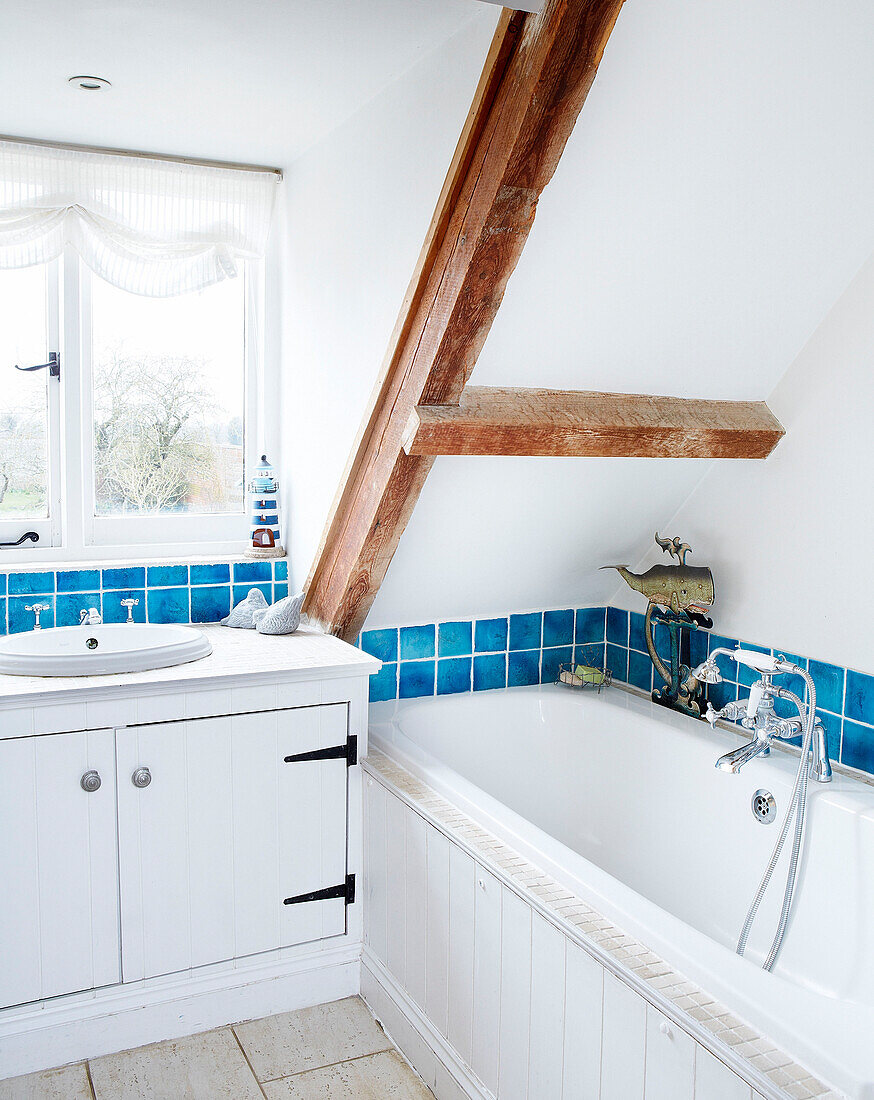 Weißes Badezimmer im Dachgeschoss mit Deckenbalken und blauen Kacheln in einer umgebauten Scheune in Nottinghamshire, England