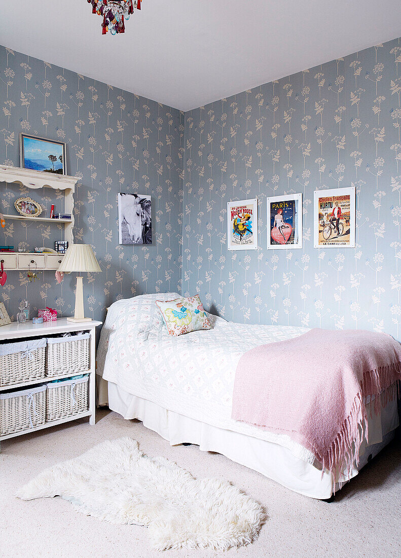 Single bed with pink blanket and patterned wallpaper in girl's room of Nottinghamshire barn conversion England UK