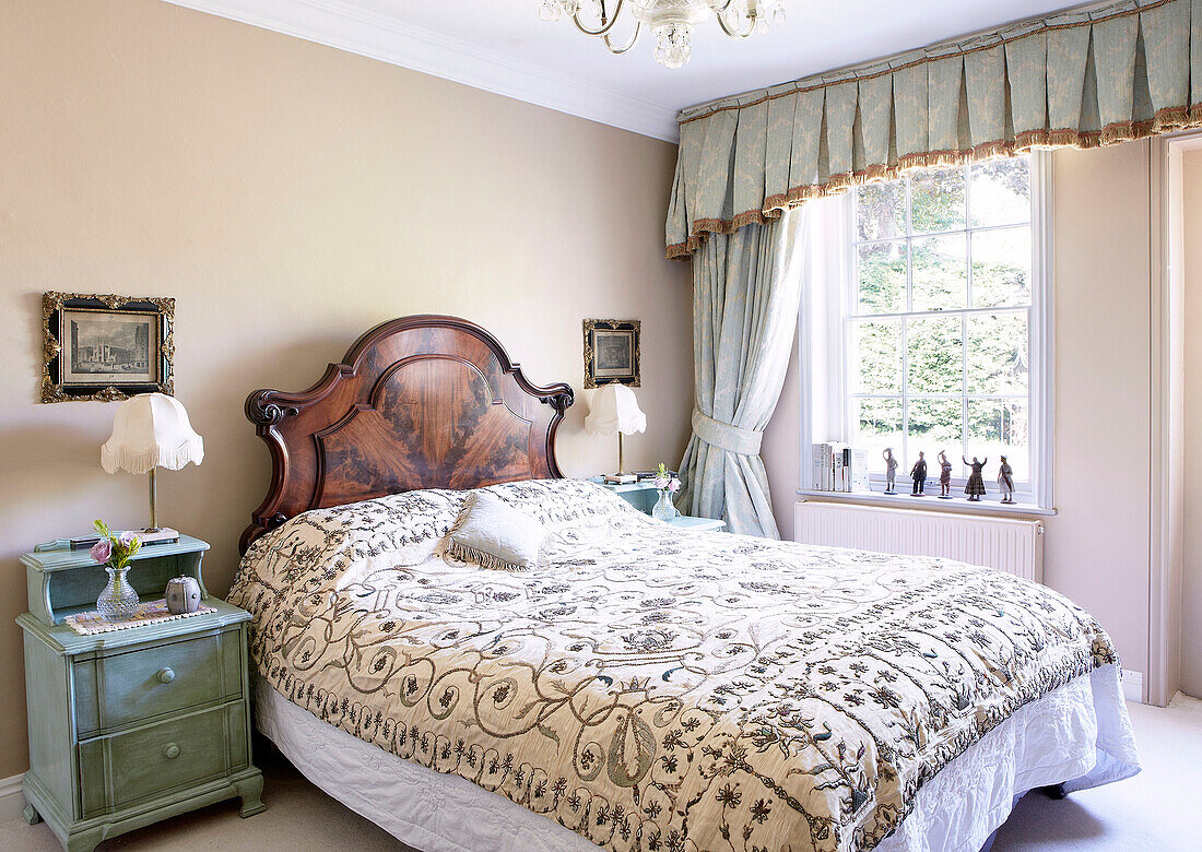 Embroidered bed cover in bedroom with curtain pelmet above window in traditional country house Welsh borders UK