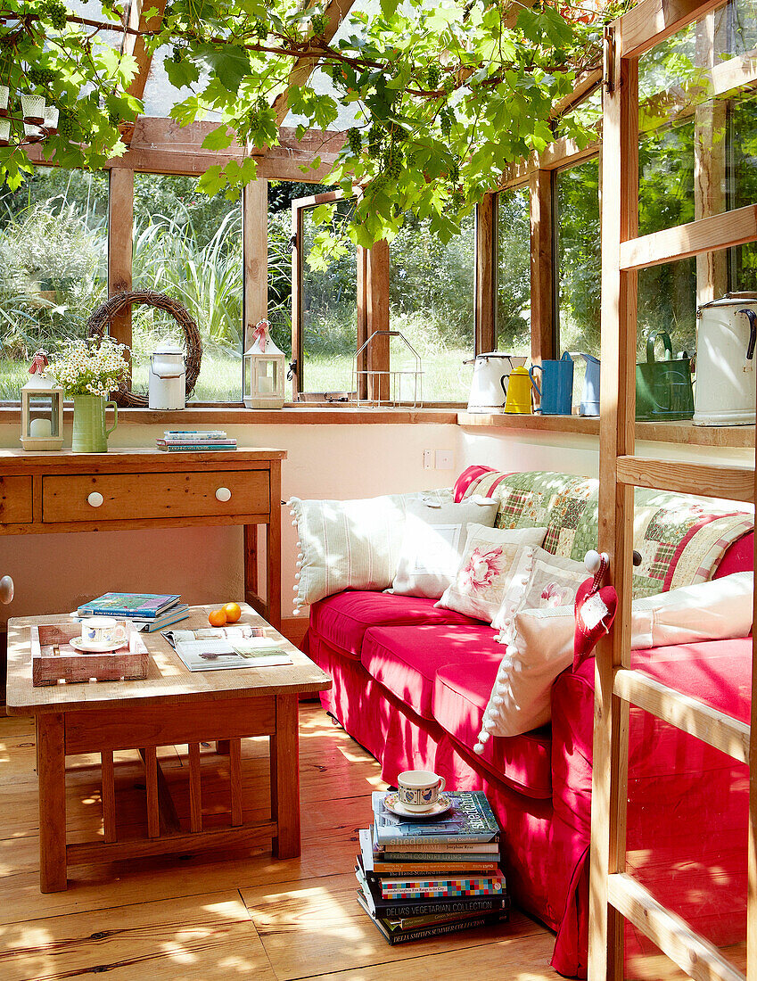 Red sofa in sunlit conservatory extension of Devonshire cottage UK