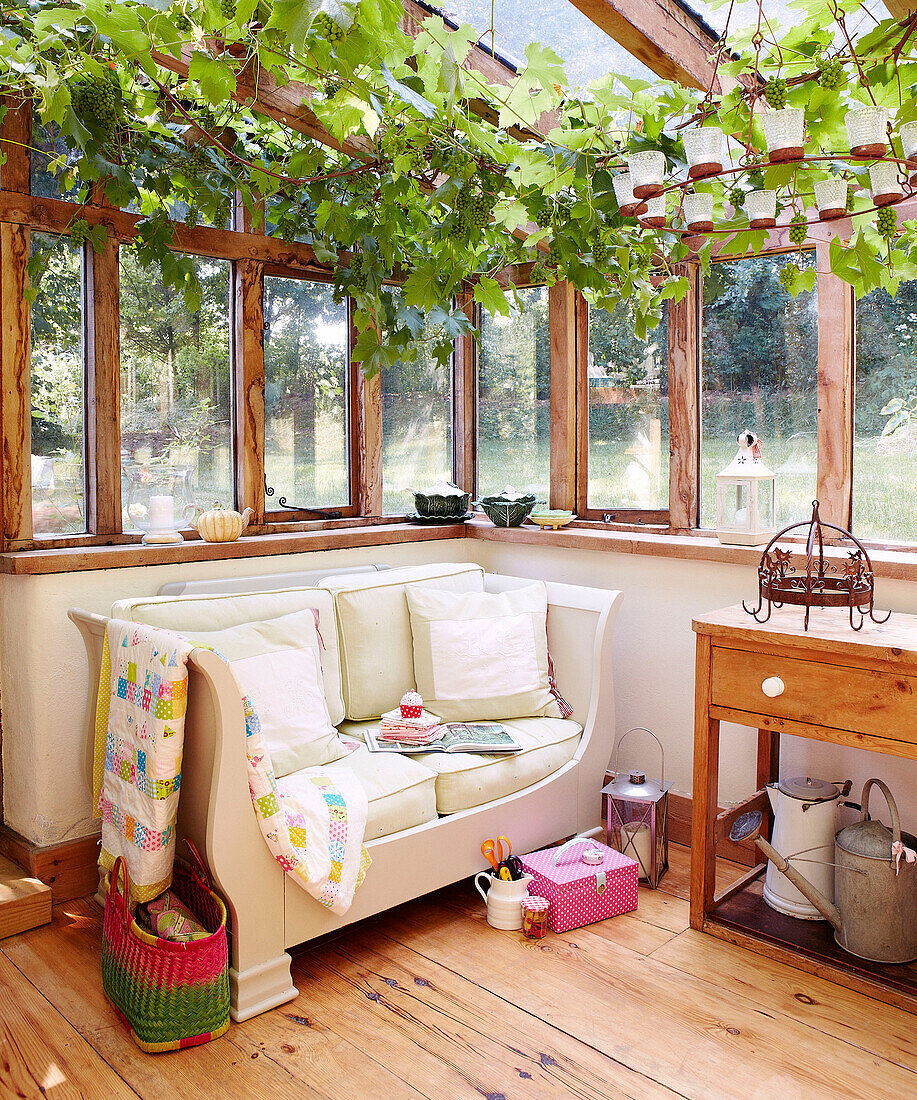 Two seater sofa under vines in conservatory extension of Devonshire cottage UK