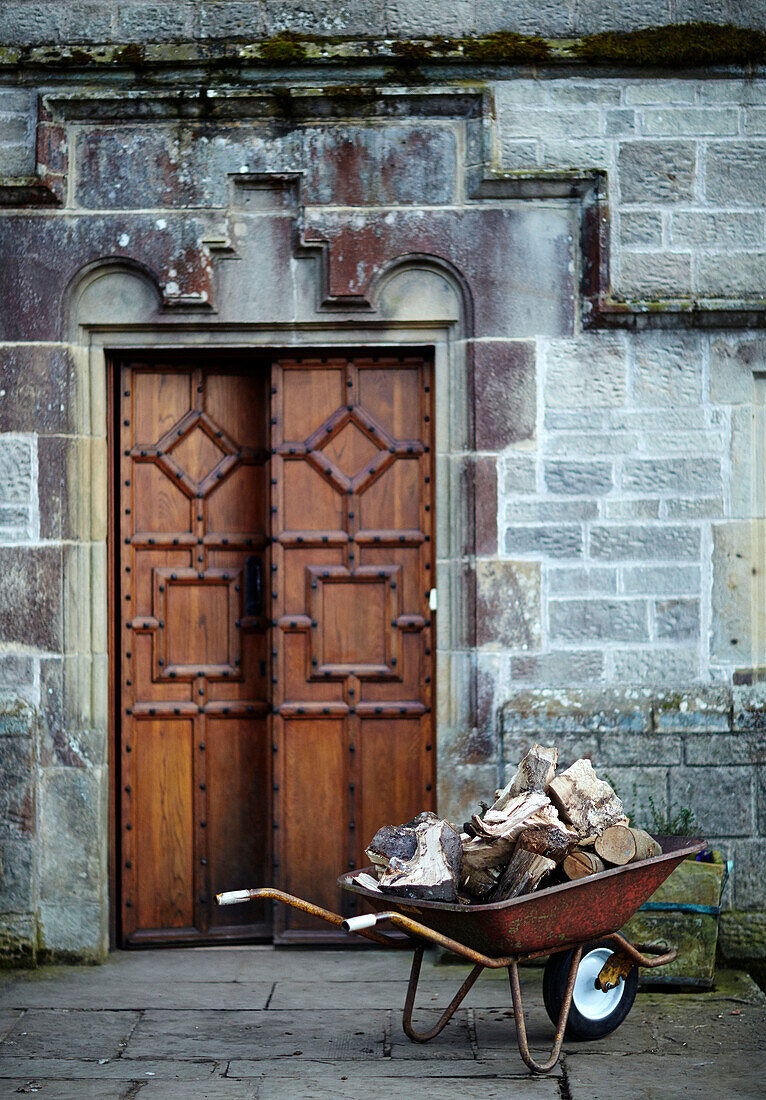 Schubkarre mit Brennholz vor den Doppeltüren eines historischen Herrenhauses in Northumbria, England, UK