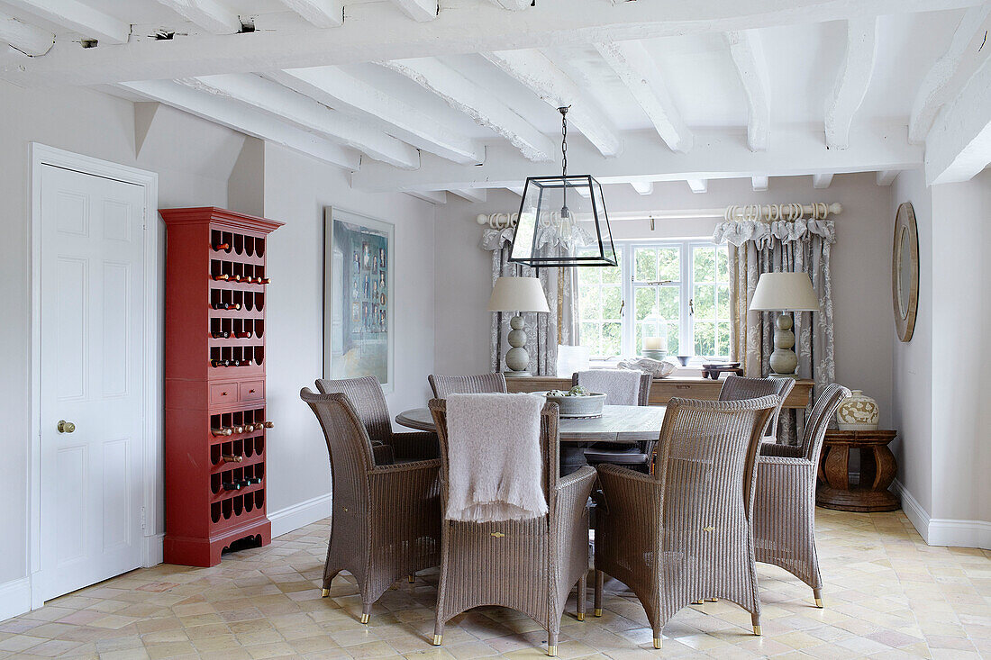 Wicker chairs at circular table with red painted wine rack in Buckinghamshire dining room UK